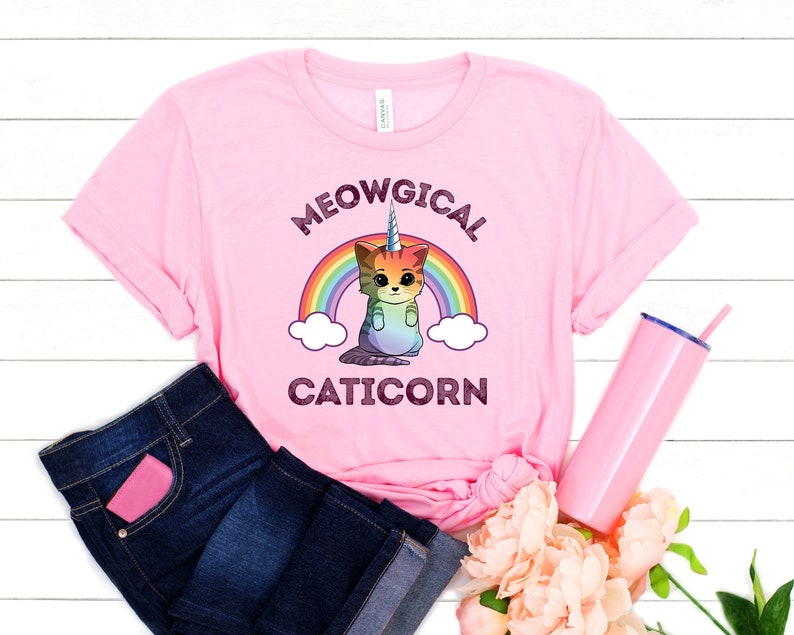 May include: Pink t-shirt with a rainbow and a cat with a unicorn horn. The text on the shirt says "MEOWGICAL CATICORN".