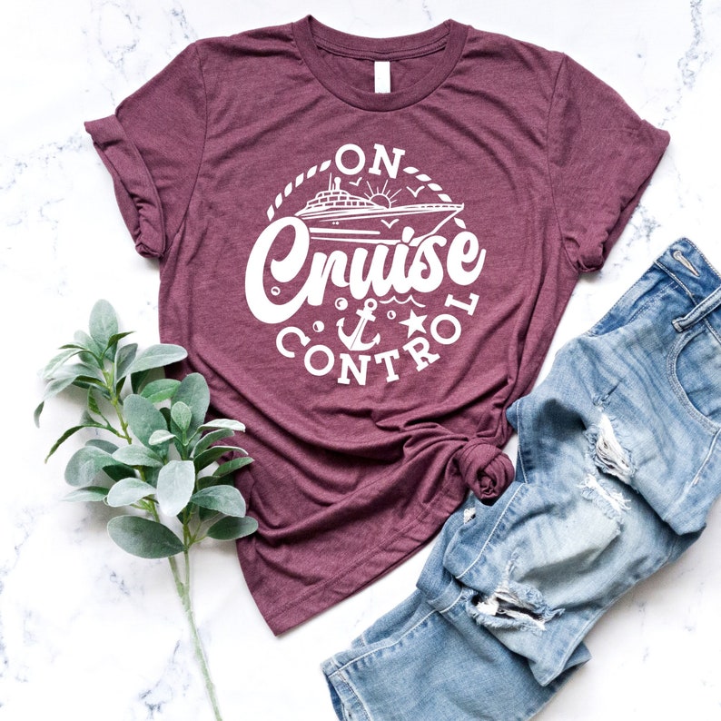 May include: A maroon t-shirt with a white graphic design that says "On Cruise Control" with a cruise ship, anchor, and star.