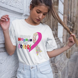 Puede incluir: Camiseta blanca con una cinta rosa hecha de cintas m&aacute;s peque&ntilde;as de colores y el texto "FIGHT CANCER IN ALL COLORS".