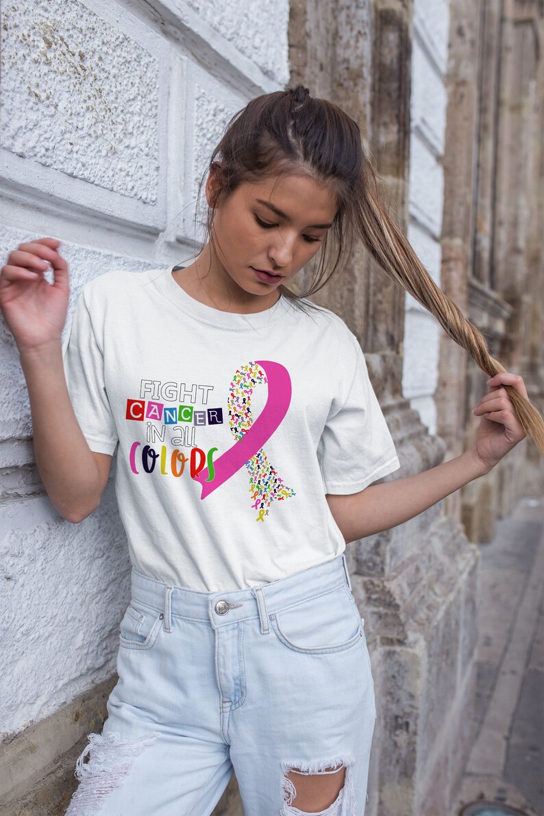 Puede incluir: Camiseta blanca con una cinta rosa hecha de cintas m&aacute;s peque&ntilde;as de colores y el texto "FIGHT CANCER IN ALL COLORS".