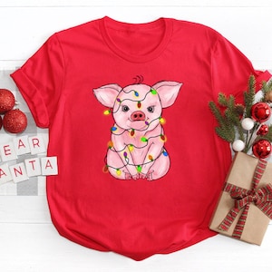May include: Red t-shirt with a pink pig wearing Christmas lights. The text "Dear Santa" is on a white background.