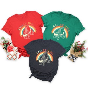 Peut inclure: Trois t-shirts avec un graphique arc-en-ciel r&eacute;tro et le texte "Roller Girl" et un dessin de patin &agrave; roulettes. Les t-shirts sont rouge, vert et gris fonc&eacute;.