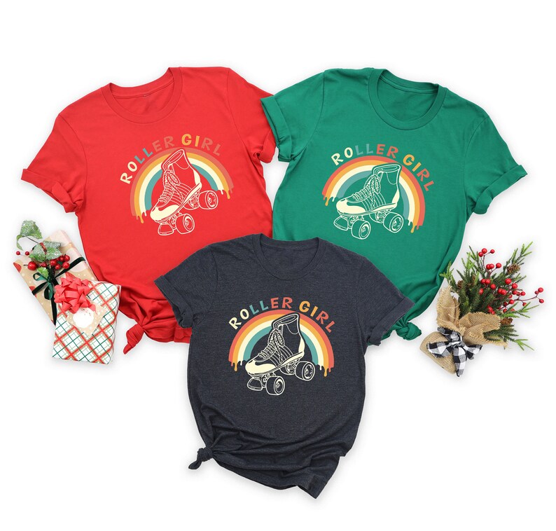 Peut inclure: Trois t-shirts avec un graphique arc-en-ciel r&eacute;tro et le texte "Roller Girl" et un dessin de patin &agrave; roulettes. Les t-shirts sont rouge, vert et gris fonc&eacute;.
