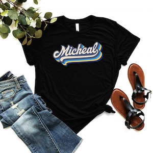Pode incluir: Camiseta preta com o nome "Micheal" escrito em uma fonte retr&ocirc; e colorida.