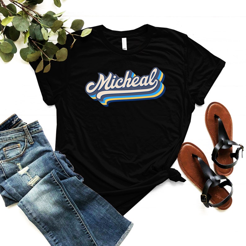 Pode incluir: Camiseta preta com o nome "Micheal" escrito em uma fonte retr&ocirc; e colorida.