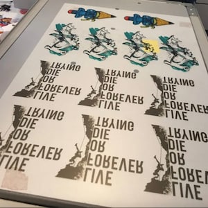 May include: A screen printing of a design with multiple repeats. The design includes a climber, a mountain, and the text "Climb Die OK Love Life". Above are cartoon images of a pencil with a rocket.