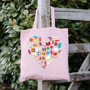 May include: A pink tote bag with a heart-shaped design made of colorful book illustrations. The bag has two handles and is made of a soft, canvas-like material.