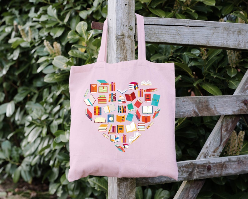 May include: A pink tote bag with a heart-shaped design made of colorful book illustrations. The bag has two handles and is made of a soft, canvas-like material.
