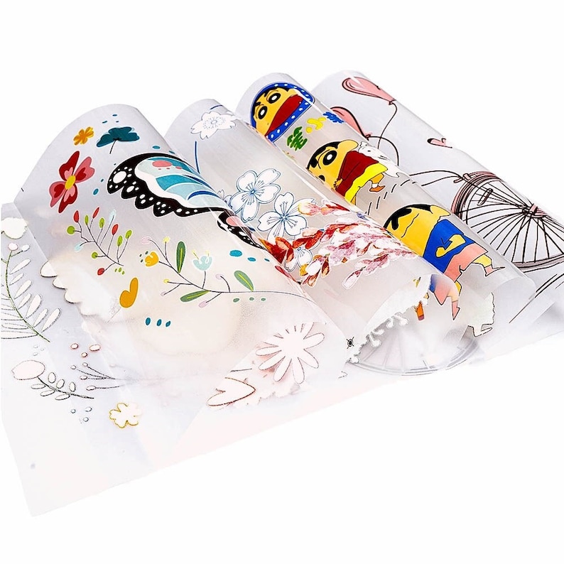 May include: Four rolled sheets of decorative paper with colorful illustrations. Designs include flowers, a butterfly, a cartoon character, and a bicycle. The paper is translucent with scalloped edges.