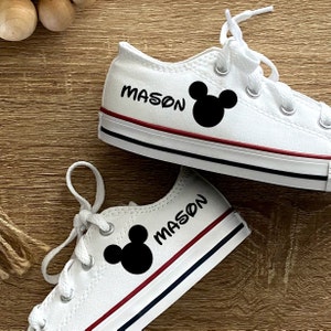 Może przedstawiać: Białe buty z pł&oacute;tna z czerwonymi i niebieskimi lam&oacute;wkami. Buty mają czarną sylwetkę Myszki Miki i napis "MASON" na nich.