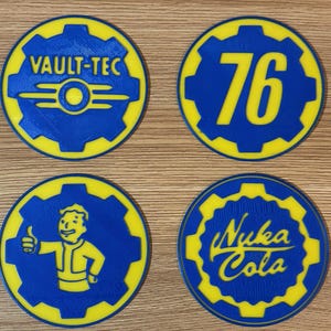 May include: Four round coasters with a blue and yellow color scheme. The coasters feature the Vault-Tec logo, the number 76, a Vault Boy character, and the Nuka-Cola logo. The coasters are likely made of a durable material.