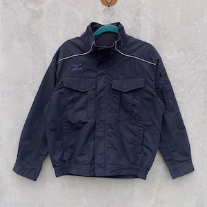 May include: Navy blue jacket with a high collar, two front pockets, and a small zippered pocket on the sleeve. The jacket has white trim and the "mizuno" logo on the chest. The jacket is hanging on a hanger.
