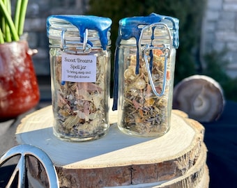 May include: Two small glass jars with blue lids filled with dried herbs and flowers. The jars are labeled "Sweet Dreams Spell Jar" and "To bring sleep and peaceful dreams".
