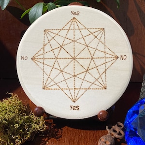 May include: A wooden circular board with a geometric design burned into the surface. The design is a star with multiple points and lines. The words "Yes" and "No" are written on the board.