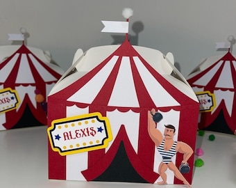 May include: Red and white striped circus tent shaped party favor box with a yellow star and the name "ALEXIS" printed on it. A cartoon strongman with a mustache is lifting weights in front of the tent.