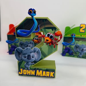 May include: Green number two party favour box featuring a koala, snake, and crab from the animated film 'Back to the Outback'. The box has the name 'John Mark' printed on the front.