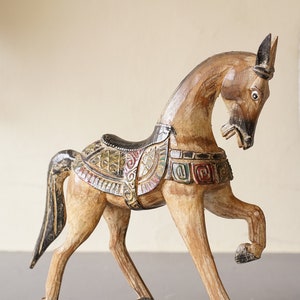 May include: Hand-carved wooden horse figurine with intricate details and colorful paint. The horse is standing on its hind legs with its head turned to the side. The saddle is decorated with geometric patterns and the horse's mane and tail are black.