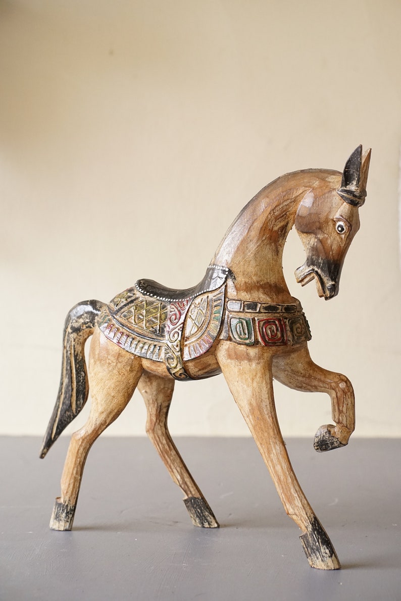 May include: Hand-carved wooden horse figurine with intricate details and colorful paint. The horse is standing on its hind legs with its head turned to the side. The saddle is decorated with geometric patterns and the horse's mane and tail are black.