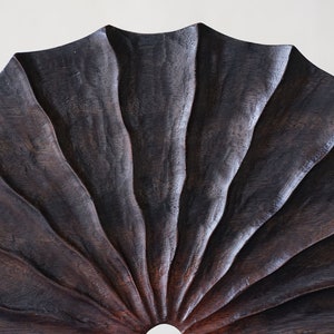 May include: A dark brown wooden fan with a scalloped edge and a circular opening in the center.