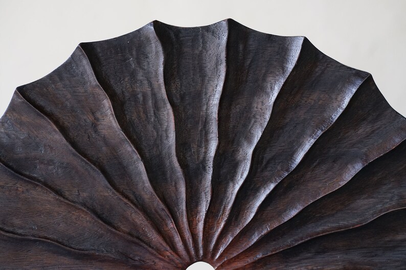 May include: A dark brown wooden fan with a scalloped edge and a circular opening in the center.
