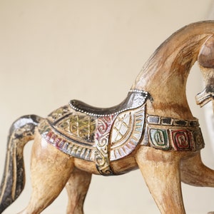 May include: A wooden horse figurine with intricate carvings and colorful paint details. The horse is standing on its hind legs with its head turned to the side. The horse is decorated with a saddle and other details.