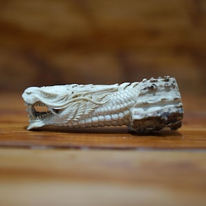 May include: A white carved dragon head on a wooden base. The dragon's mouth is open and its eyes are closed. The base is made of natural wood and has a rough texture.