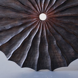 May include: A dark brown wooden wall art piece with a circular shape and a central hole. The wood is carved in a radial pattern, creating a sunburst effect.