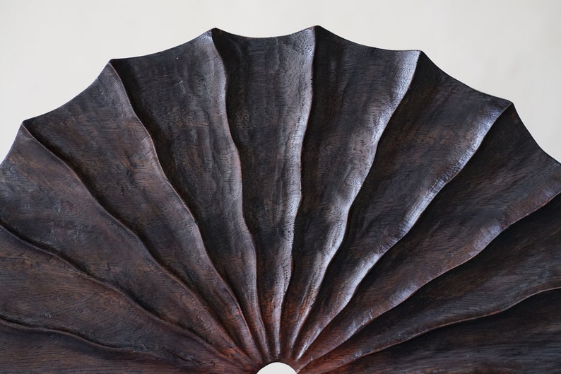 May include: A dark brown wooden fan with a scalloped edge and a circular opening in the center.