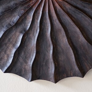 May include: A dark wood wall sculpture with a fan-like design. The wood is carved with a series of concentric circles, creating a ripple effect.