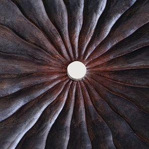 May include: A close-up of a dark brown wooden surface with a circular, white, raised design in the center. The surface has a radial pattern of grooves radiating outward from the center.