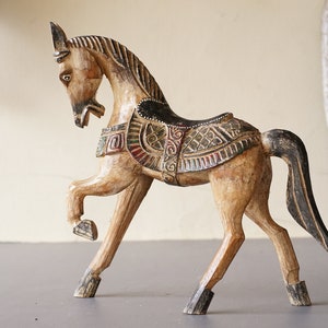 May include: A hand-carved wooden horse figurine with intricate details and colorful paint. The horse is standing on all four legs with its head turned to the side. The horse is decorated with a saddle and other embellishments.