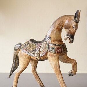 May include: Hand-carved wooden horse figurine with intricate details and colorful paint. The horse is standing on its hind legs with its head turned to the side. The saddle is decorated with geometric patterns and the horse's mane and tail are painted black.