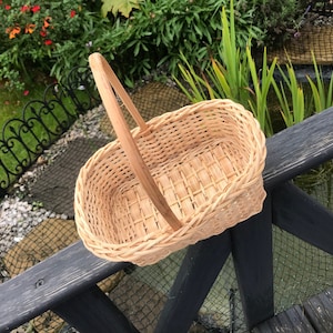 May include: A natural woven wicker basket with a handle. The basket is oval shaped and has a light brown colour.
