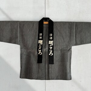 May include: A black and white striped work jacket with a black sash that has white Japanese characters on it. The characters read "清酒 昭  う  つ  "