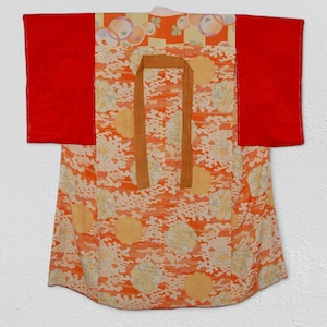Può includere: Un kimono giapponese tradizionale con un motivo floreale rosso e arancione. Il kimono ha una cintura marrone e maniche rosse.
