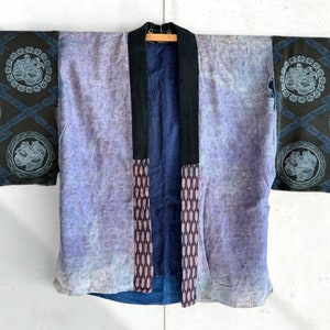 Op de afbeelding: Een vintage Japanse indigo-gekleurde katoenen kimono met een donkerblauw en zwart geometrisch patroon op de mouwen. De kimono heeft een vervaagde blauwe en paarse kleur en een donkerblauw en wit geometrisch patroon aan de voorkant.