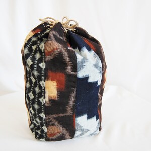 Op de afbeelding: Een bruine, blauwe en witte gepatroneerde trekkoordtas gemaakt van stof. De tas is vastgebonden met een bruin koord.