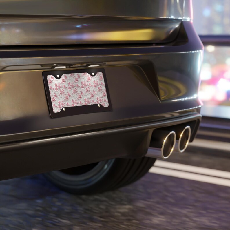 May include: A black car with a pink and white patterned license plate frame. The frame is attached to the rear bumper of the car.