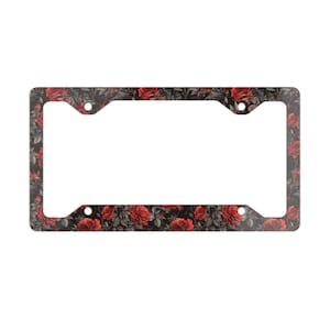 May include: License plate frame with a floral pattern of red roses and gray leaves on a black background. The frame has a rectangular shape with four mounting holes and a white space for the license plate.