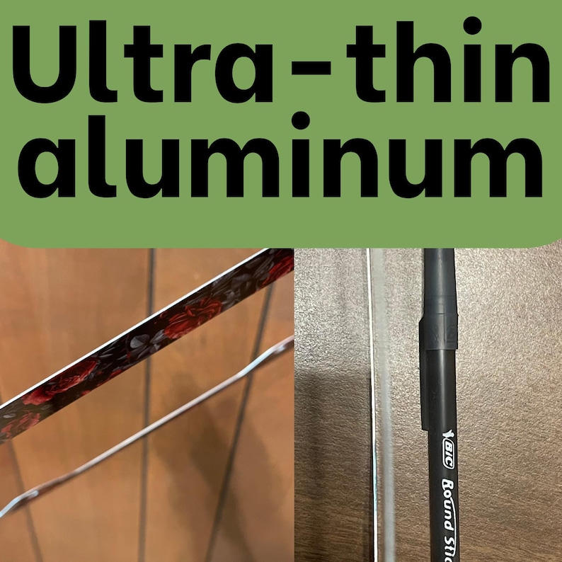 Op de afbeelding: Een ultra-dunne aluminium plaat met een donker bloemenpatroon met rode rozen aan &eacute;&eacute;n kant en een metalen rand. Een zwarte Bic Round Stic pen is verticaal naast de rand geplaatst om het dunne profiel van het materiaal te demonstreren.
