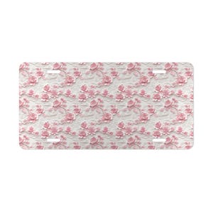 May include: A white license plate with a pink floral pattern. The flowers are embossed and have a 3D effect.