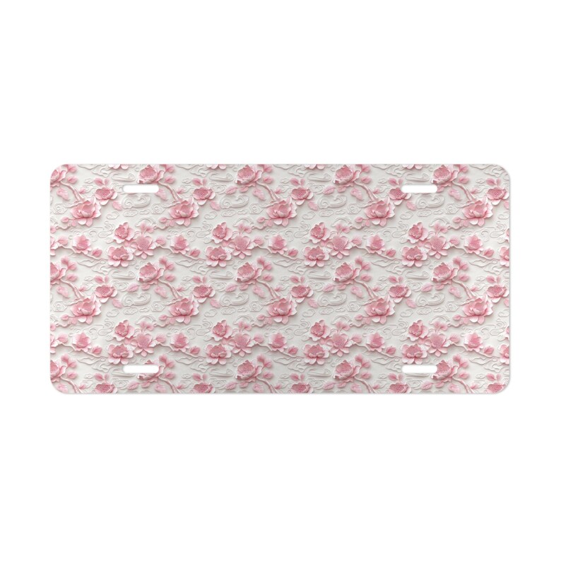 May include: A white license plate with a pink floral pattern. The flowers are embossed and have a 3D effect.