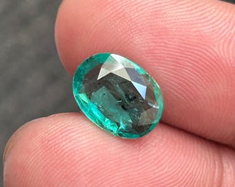 May include: Oval-shaped, faceted teal gemstone. The gem's facets catch the light, producing a sparkling effect. The stone is held between fingers, highlighting its size and clarity. Suitable for jewellery making.
