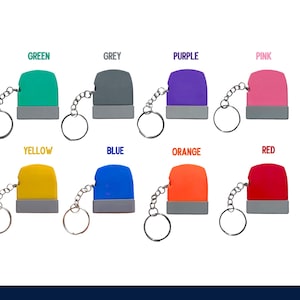 May include: Eight colourful keychain stamps in green, grey, purple, pink, yellow, blue, orange, and red. Each stamp has a silver chain and ring. The colours are labelled above each stamp.