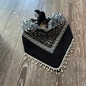 Puede incluir: Bandana negra con un patrón paisley blanco y flecos de pedrería plateados.