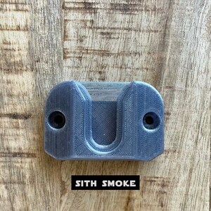 May include: A gray plastic wall mount with two screw holes and a U-shaped cutout. The text "SITH SMOKE" is printed below the mount.