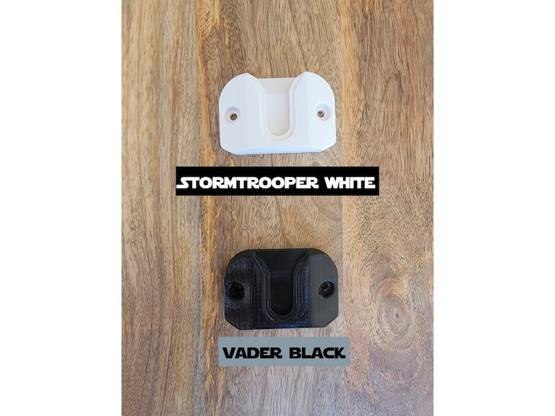 May include: Two 3D printed wall mounts for a lightsaber. One is white and labeled "STORMTROOPER WHITE". The other is black and labeled "VADER BLACK".