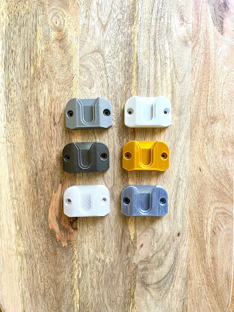 May include: Six wall mounts in different colors: gray, white, black, gold, white, and blue. The mounts are made of plastic and have a rectangular shape with a curved top.