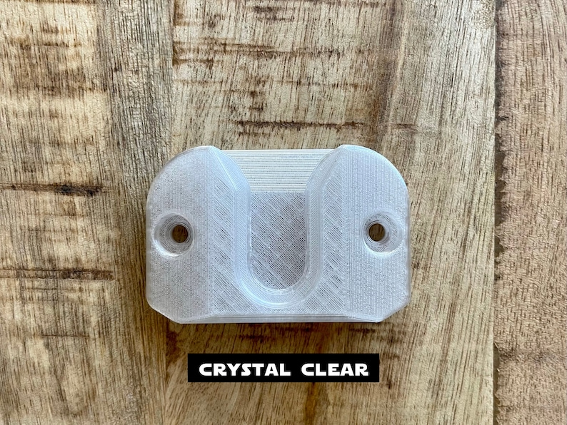 May include: A clear plastic wall mount with two holes for screws. The mount has a U-shaped opening in the center.