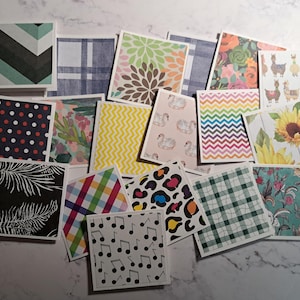 May include: A collection of square cards with various patterns and designs. The cards feature floral, geometric, and animal prints, including polka dots, chevrons, and llamas. The color palette includes blues, greens, yellows, and pinks.